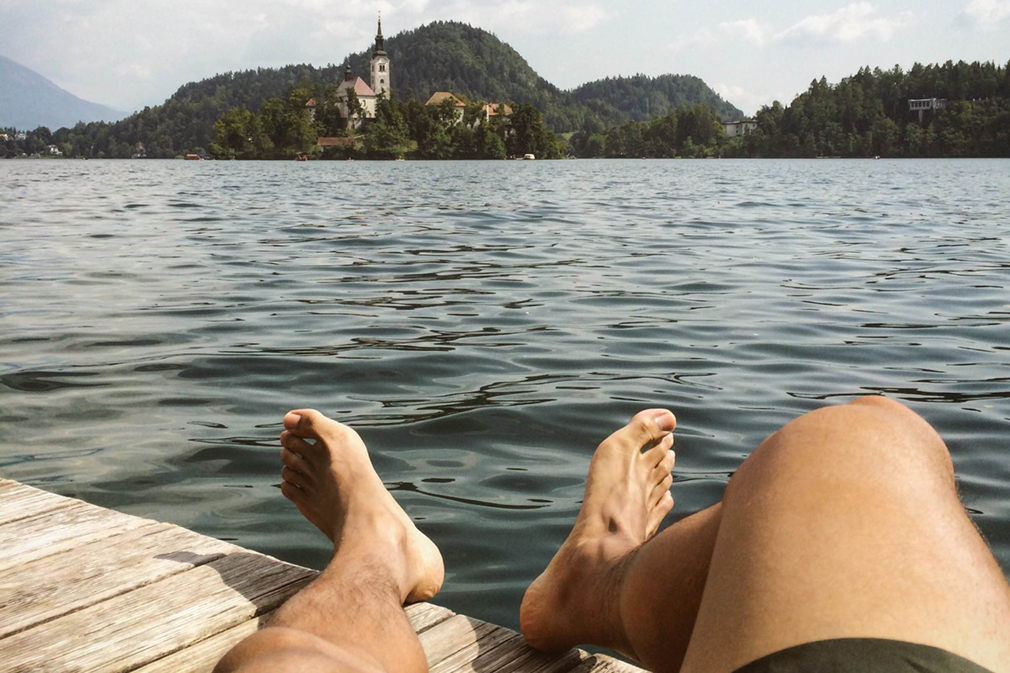 A pair of feet outstretched on a lakeside dock with a chapel in the distance