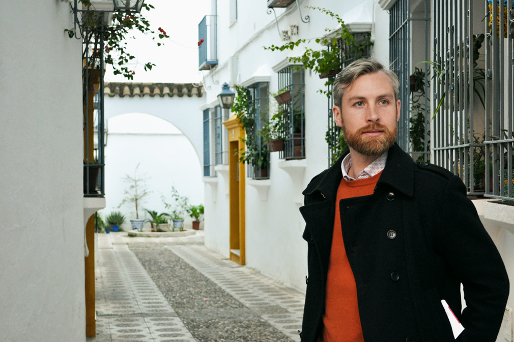 Man in a narrow alleyway with white buildings and hanging plants