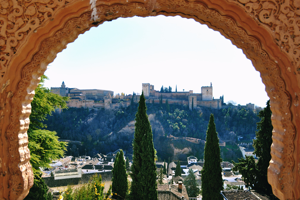 Panorama of the fortress of the Alhambra as seen through an intricate stucco archway