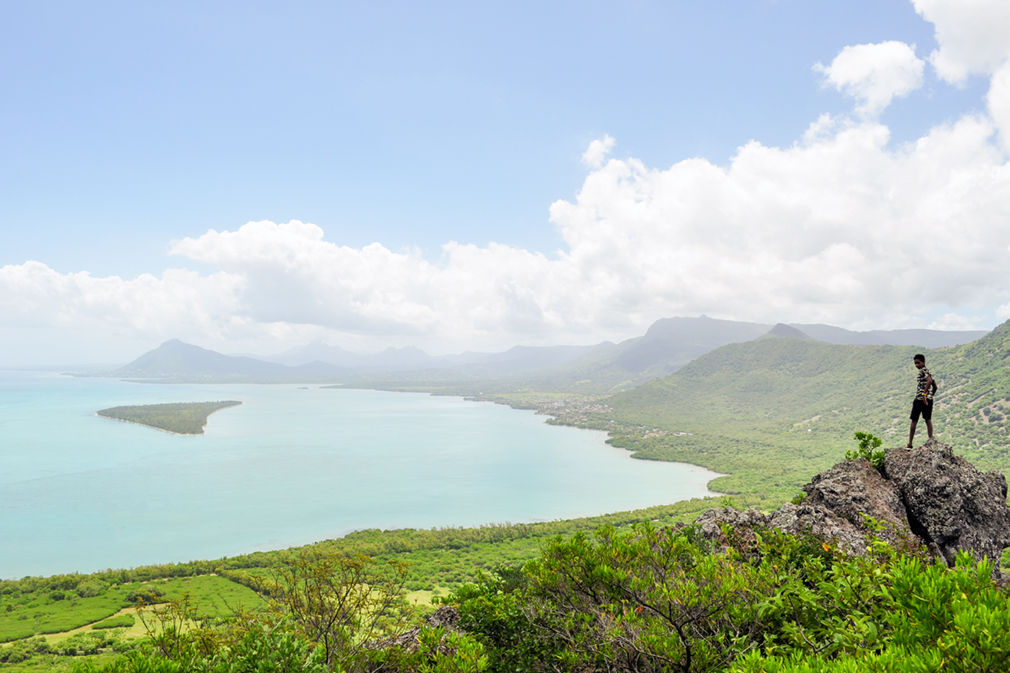 Boy standing on a rock with a panoramic view of mountains and the ocean