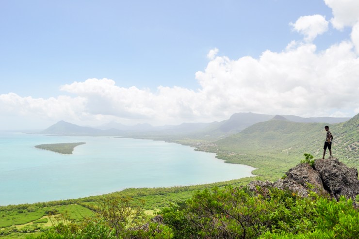 Boy standing on a rock with a panoramic view of mountains and the ocean