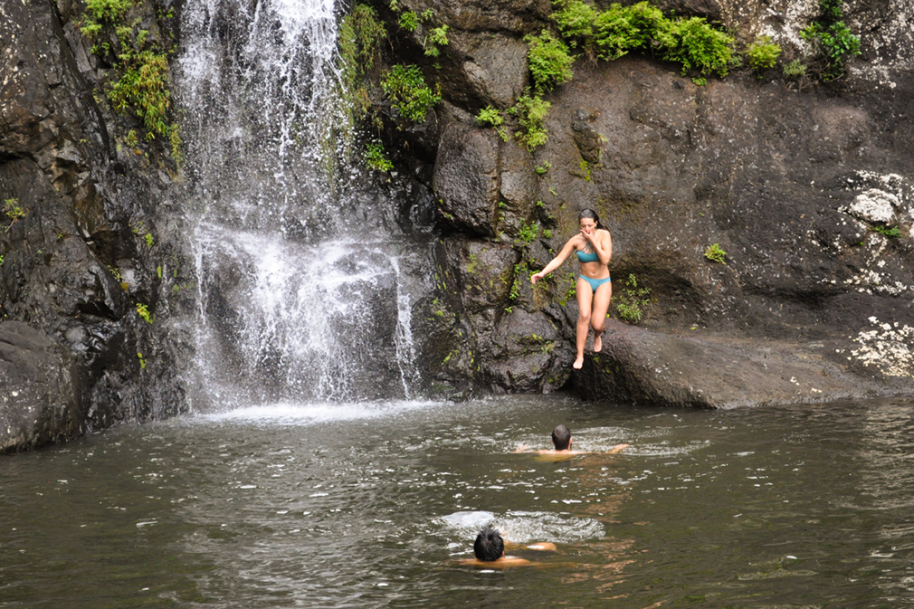 Young woman jumping into the pool of a waterfall
