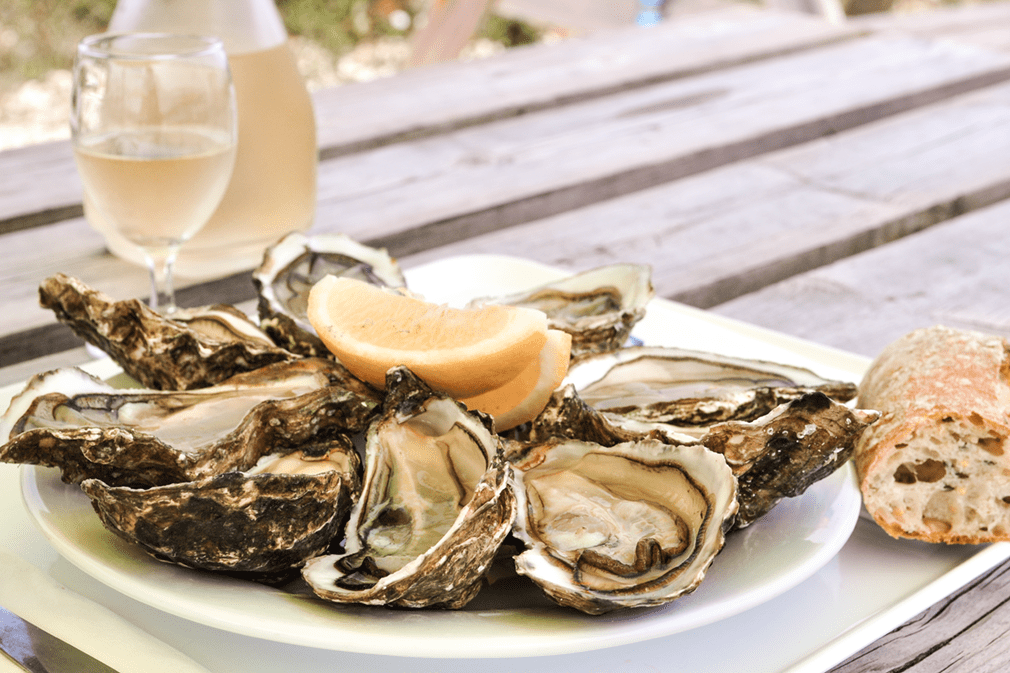 A plate of oysters on half shell paired with bread, lemon wedges, and white wine