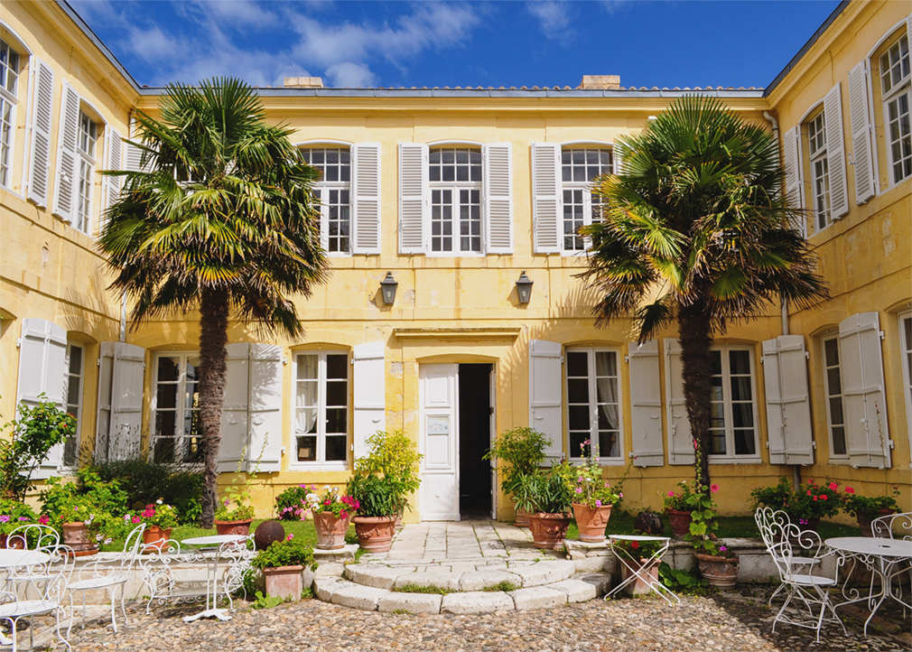 Front view of an 18th century mansion with decorative palm trees and plants