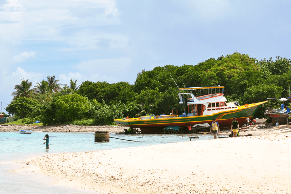 A colorful fishing boat is being repaired on a tropical beach