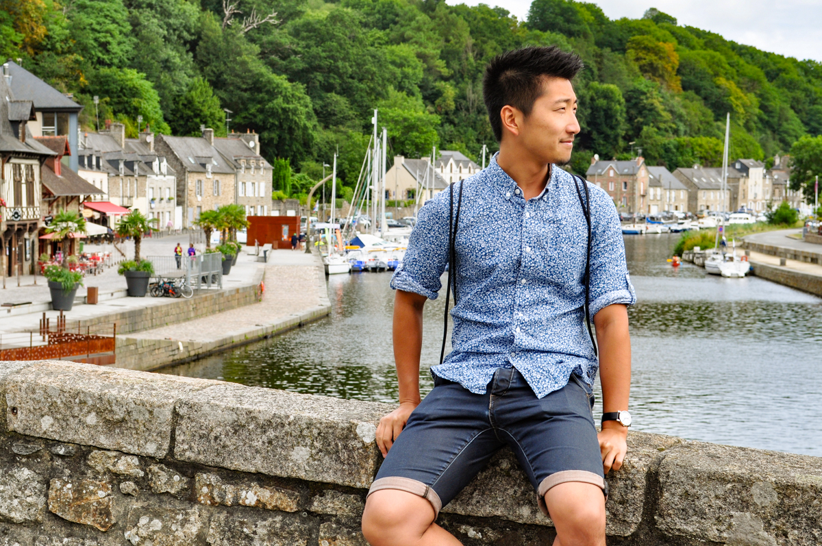 Man sitting on bridge in front of row of stone houses and trees