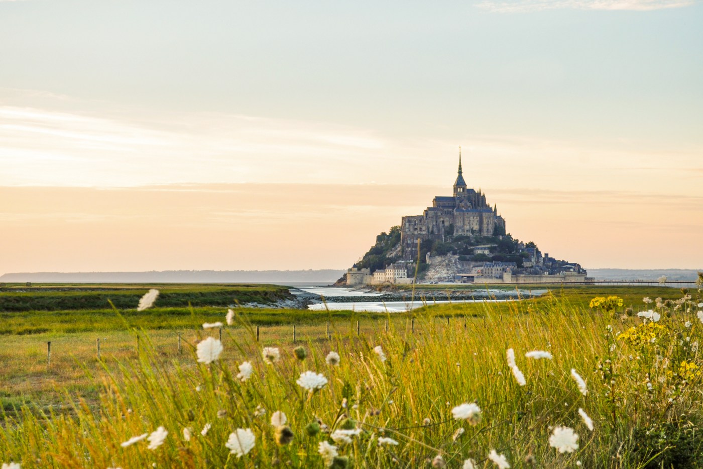 A rocky islet and monastery and green fields at sunset