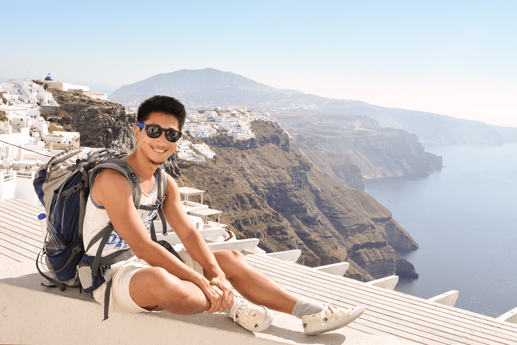 Smiling man in sunglasses and shorts on a white balcony in front of high cliffs
