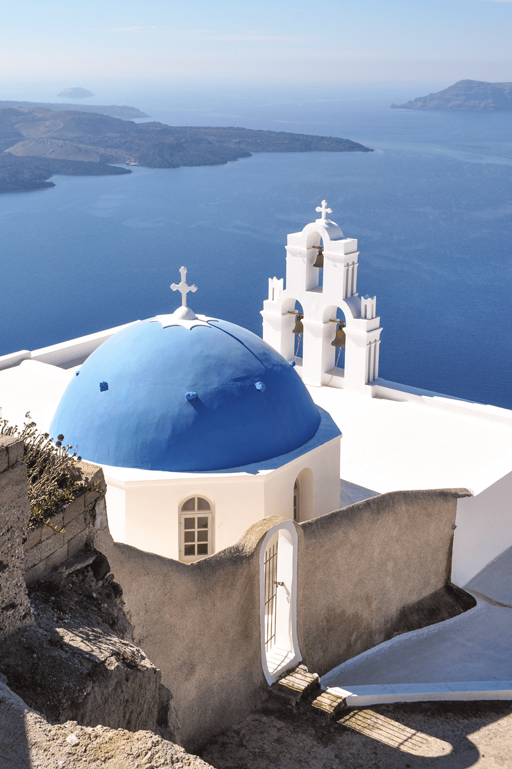 Blue-domed church with three bells overlooking the sea