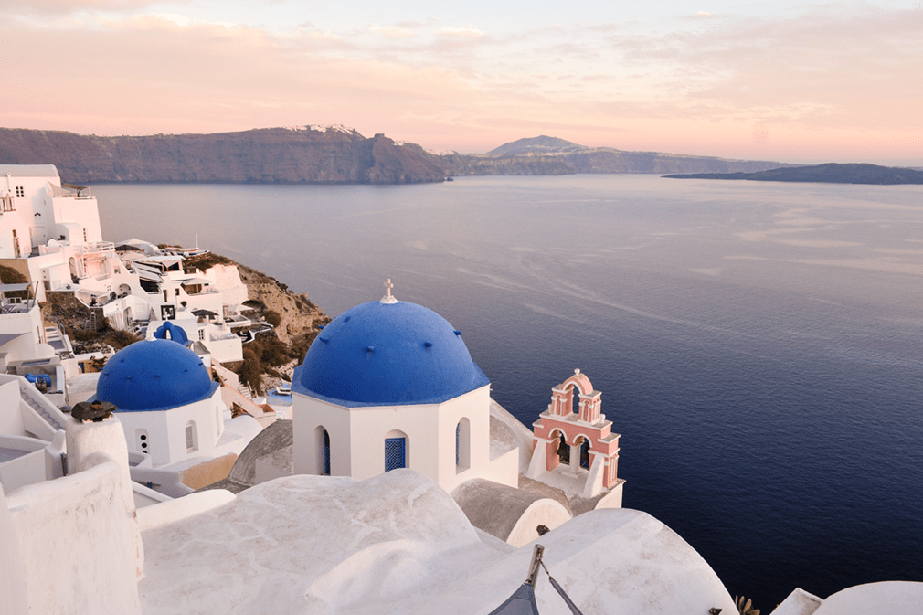 Blue-domed churches and white buildings on clifftop in sunset