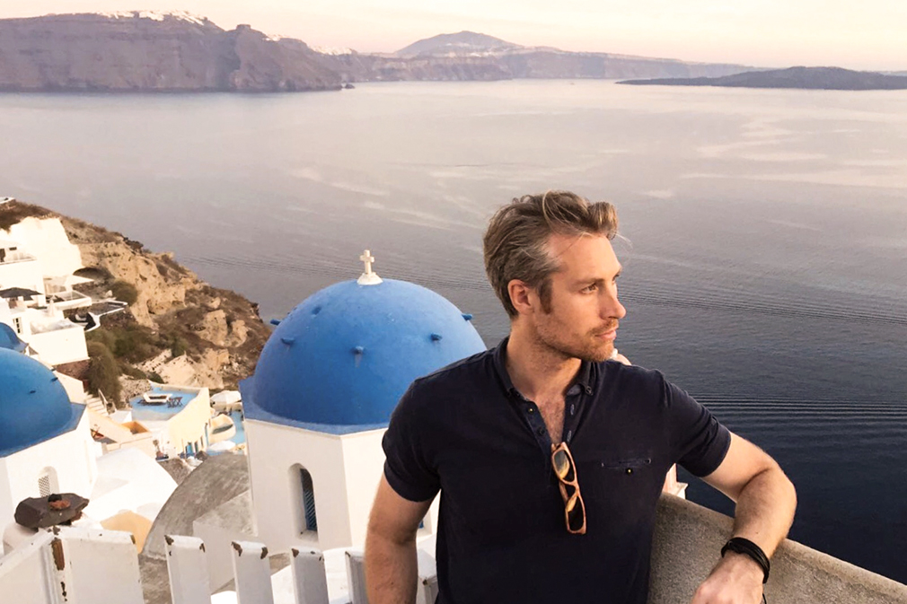 Man in front of blue-domed church and open water at sunset