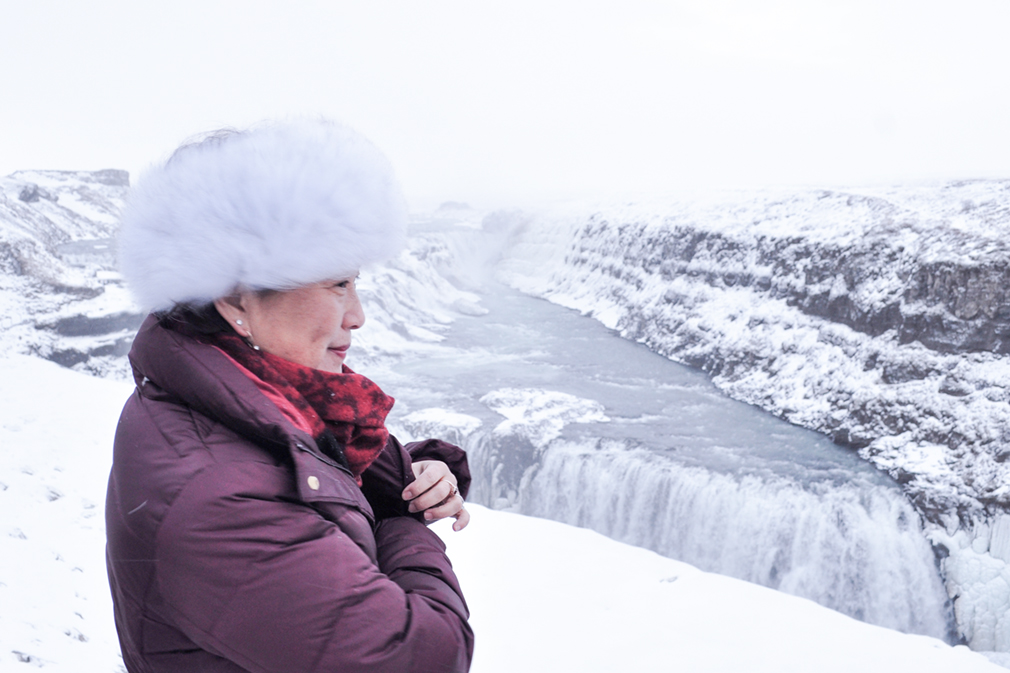 Woman in winter clothing standing by a partially frozen waterfall
