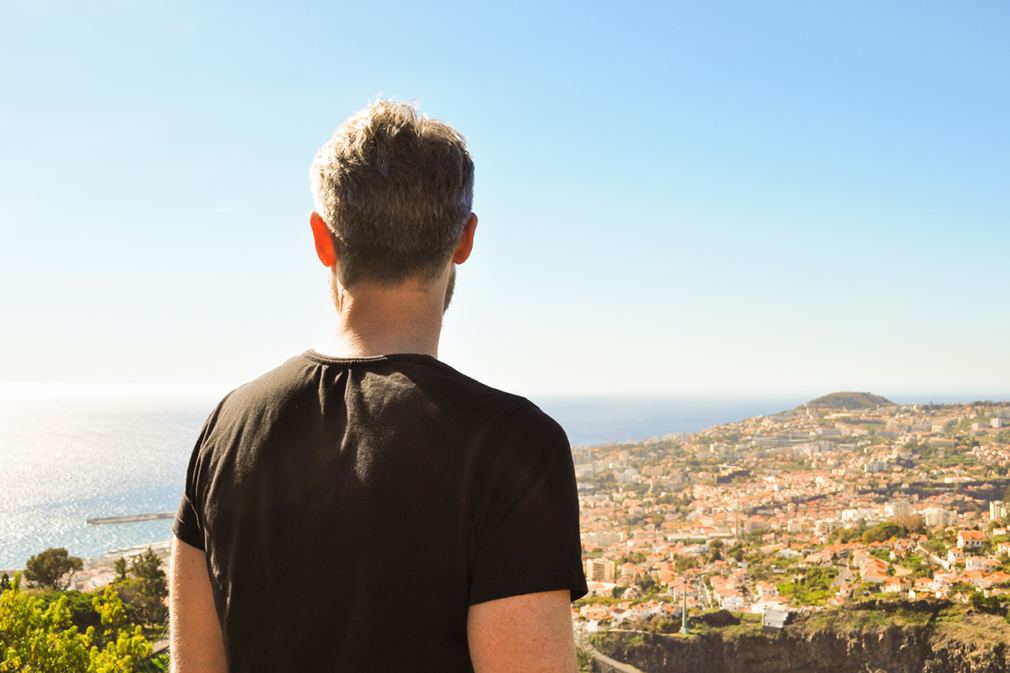 Man in black shirt looking over a city and the ocean