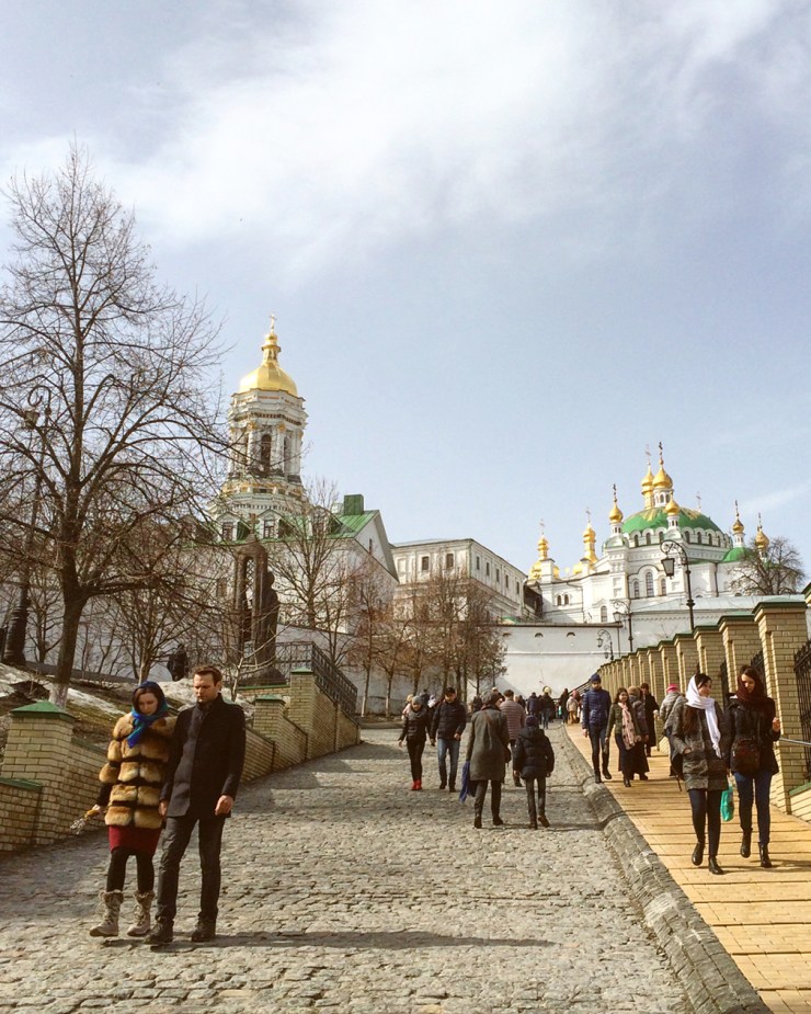 People promenading down the sloping hill of a monastery with golden spires and green domes