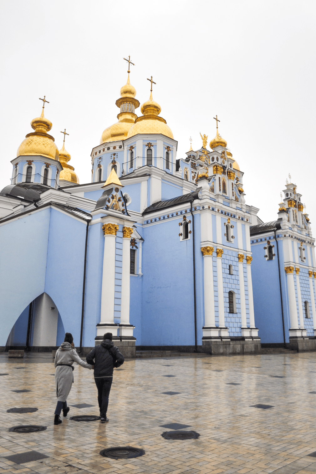 A couple walking in front of a blue cathedral with golden domes