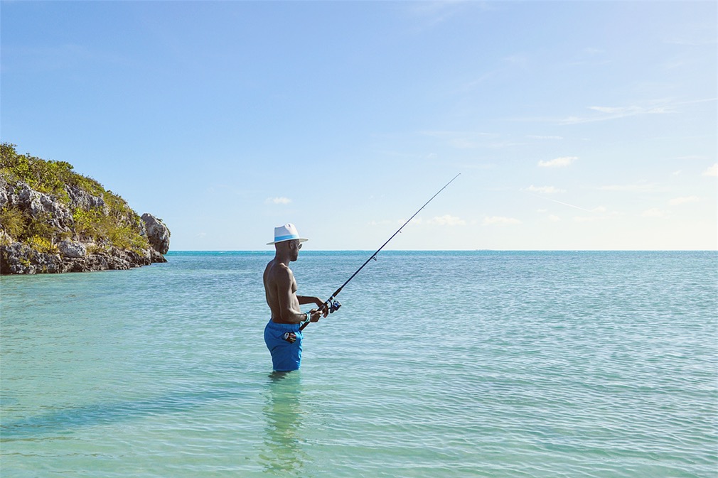 Man in hat and blue swim shorts fishing in ocean