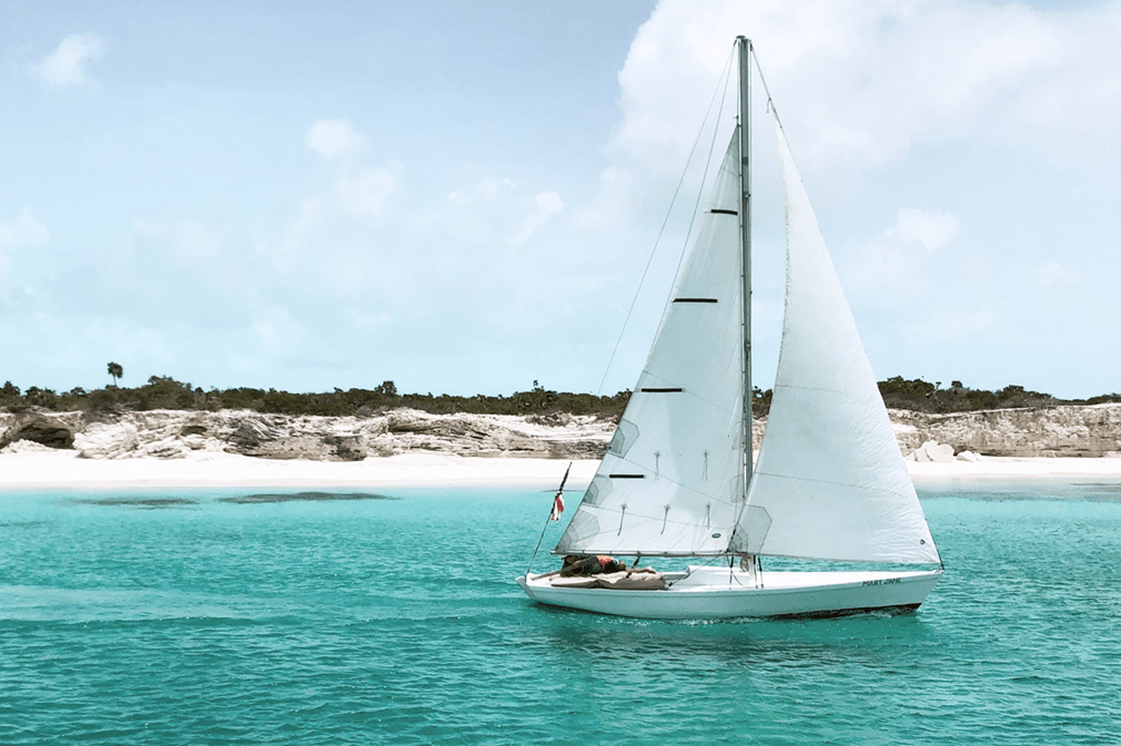 A sailboat gliding in tranquil waters along the shore of a cay