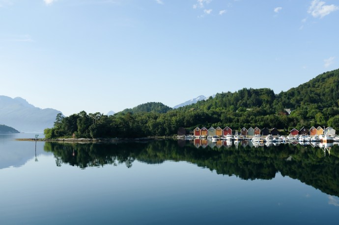 A fjord landscape with colorful boathouses and their mirror reflection