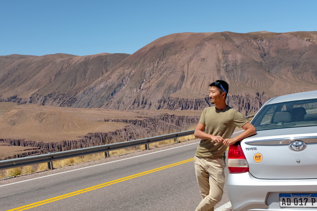 Man posing by car in front of canyon landscape