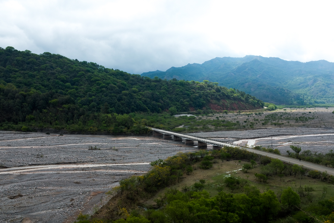 A bridge crossing a dried out river in a jungle-clad valley landscape