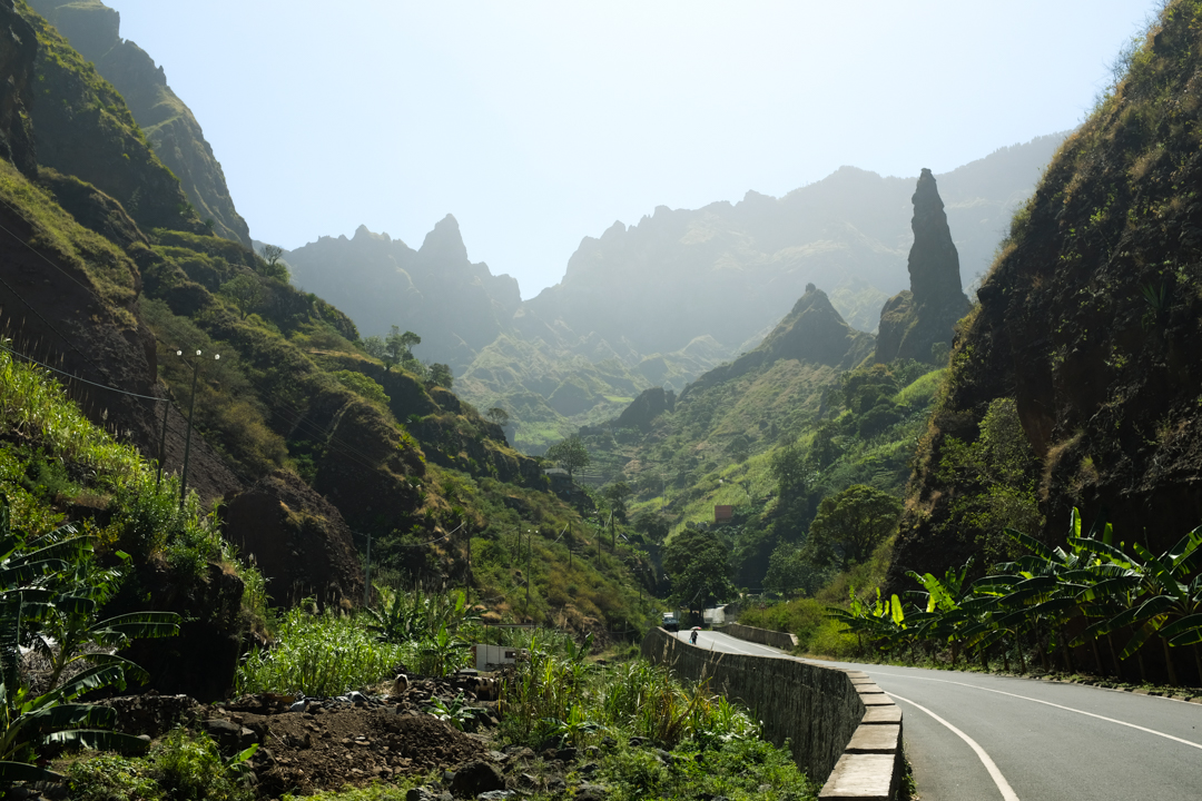 A paved road leading into a green, mountainous valley