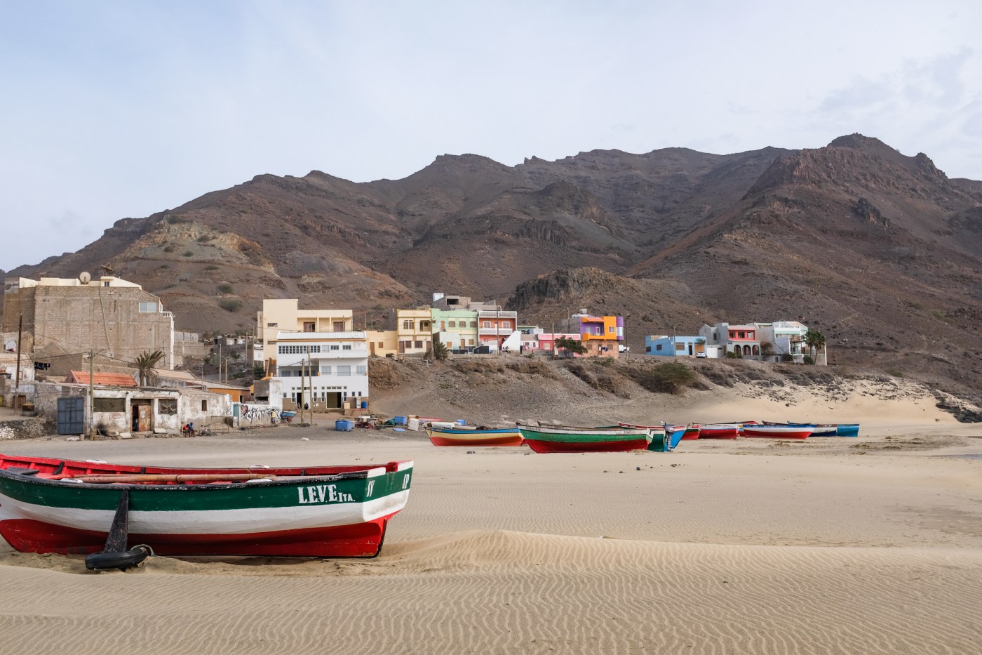 Painted boats on a sandy beach in front of a small fishing village