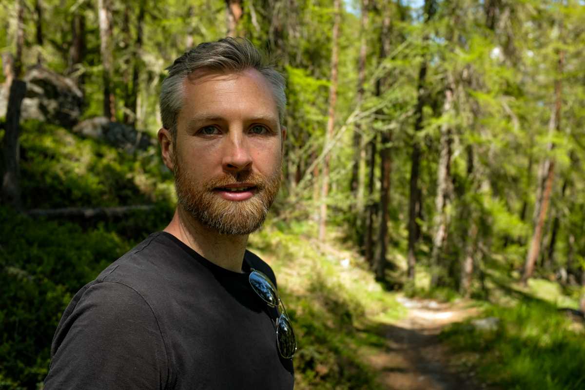A man looking into the camera on a forested path