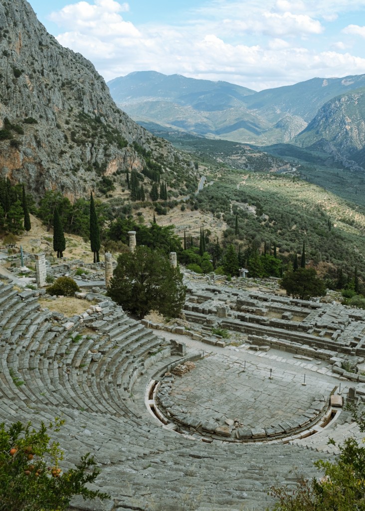 The ruins of an amphitheater and a temple against a valley backdrop