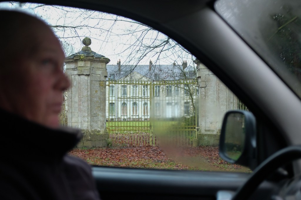 Man sitting in car in front of gated chateau
