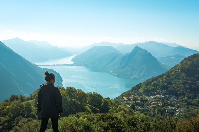 A woman looks over a rustic mountain village above a large lake