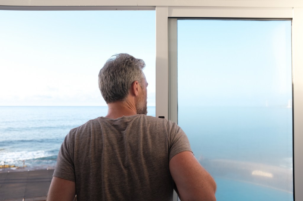 A man looks out a window at the ocean
