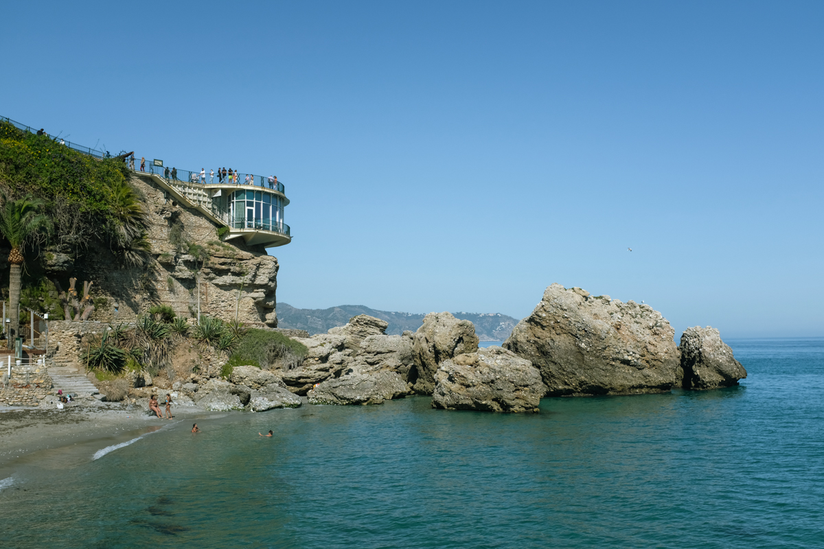 A glass building atop a rocky promontory by the beach