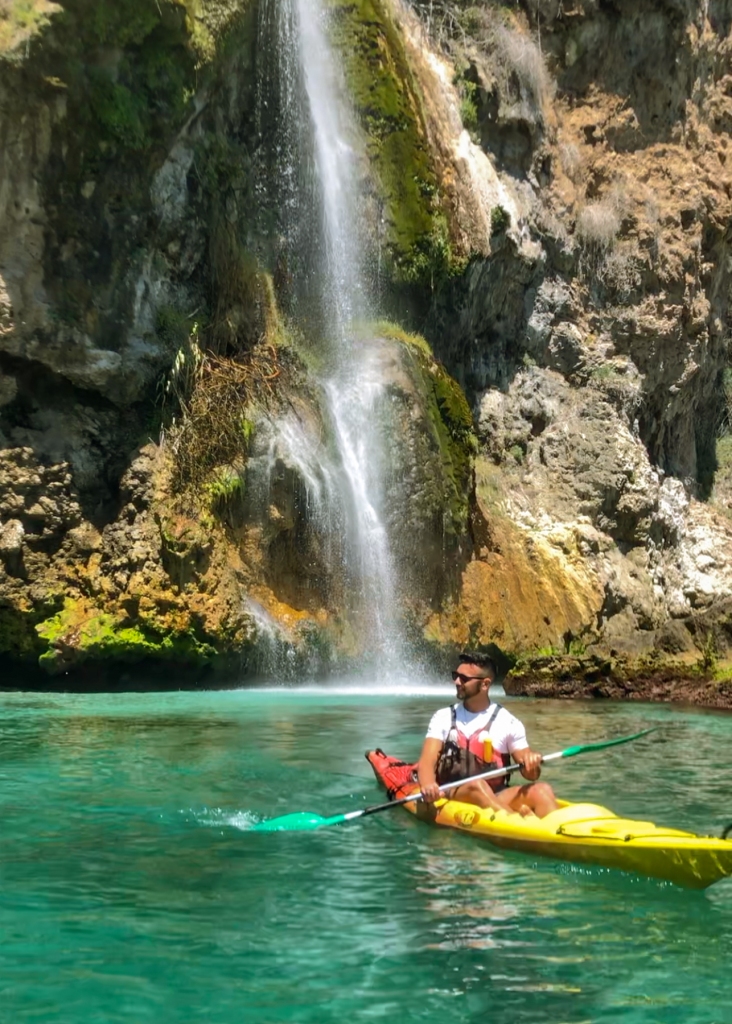 A man in a kayak resting by a waterfall