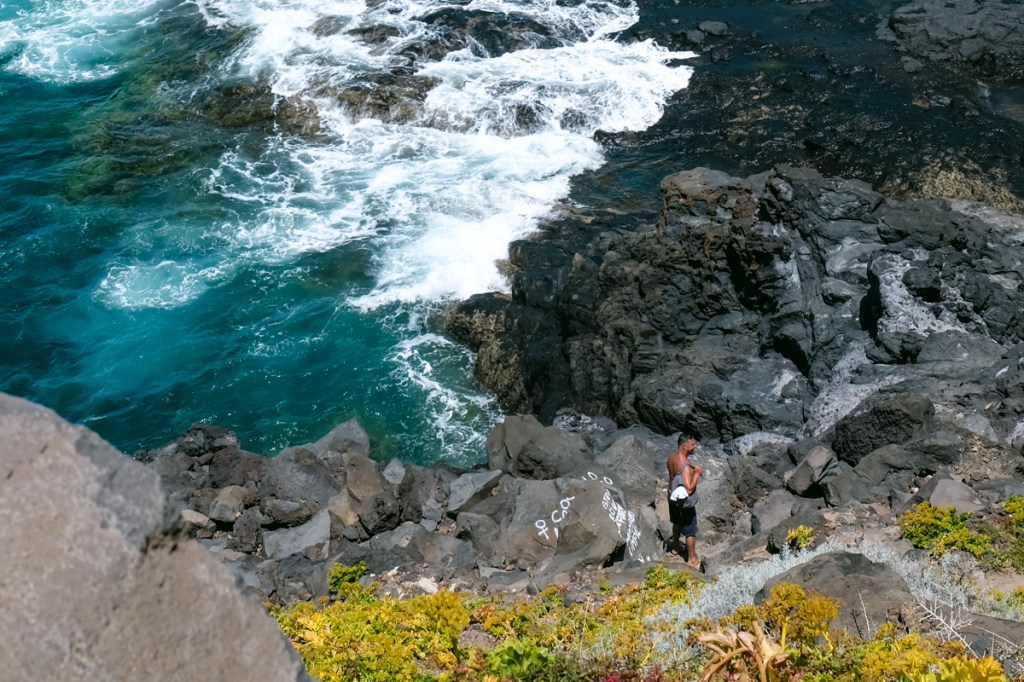 A man carrying a sac makes his way down to a natural rock pool