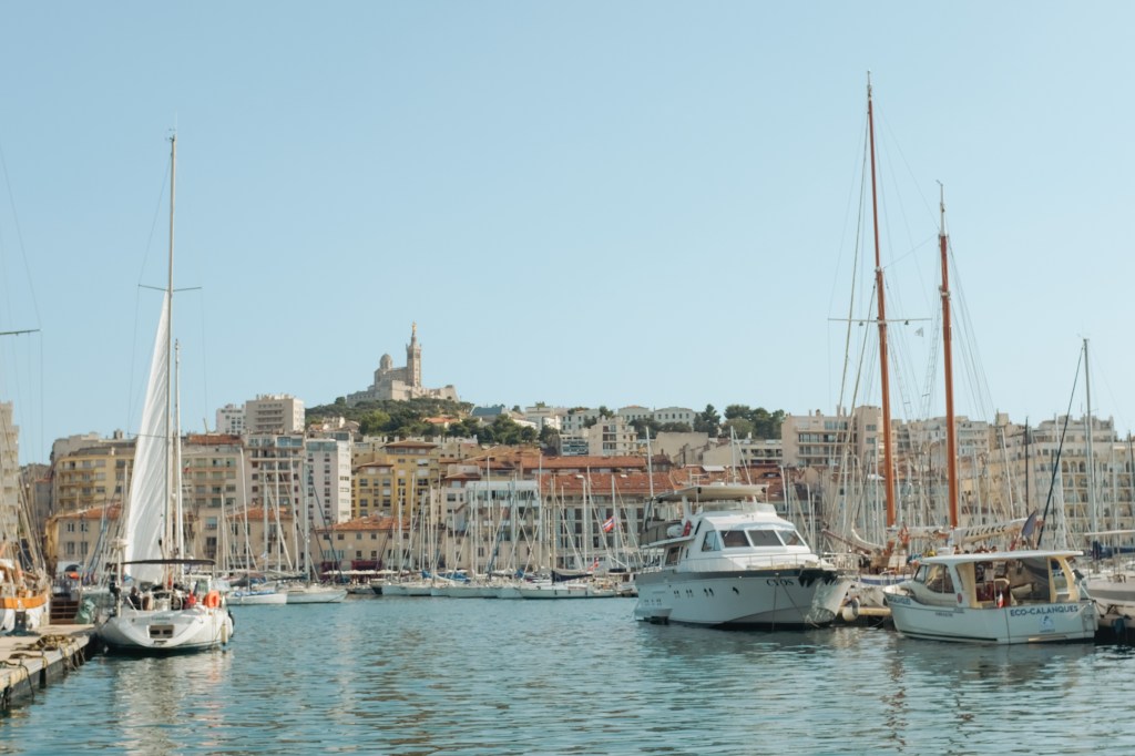 European harbor with a basilica atop a green hill in the distance