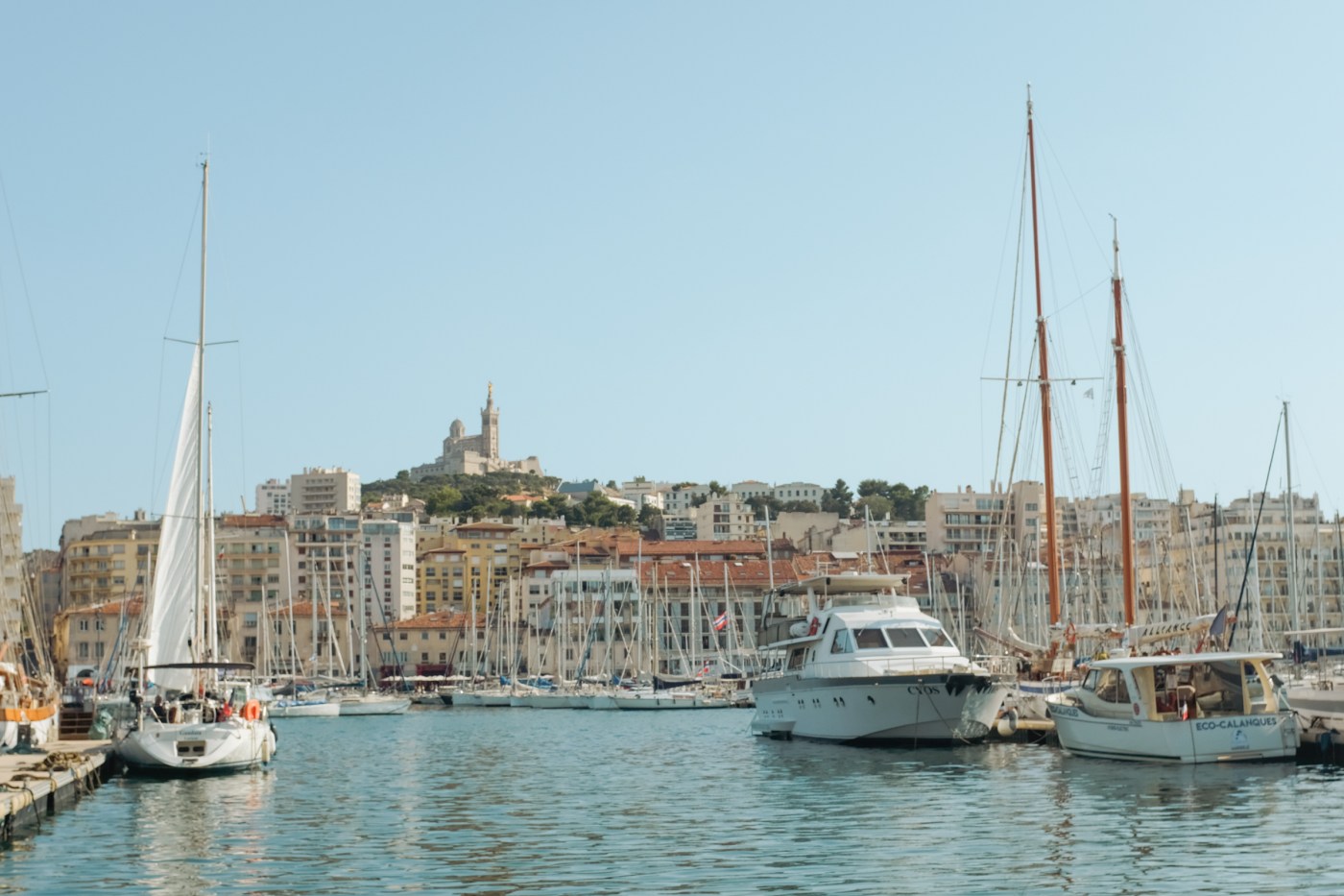 European harbor with a basilica atop a green hill in the distance