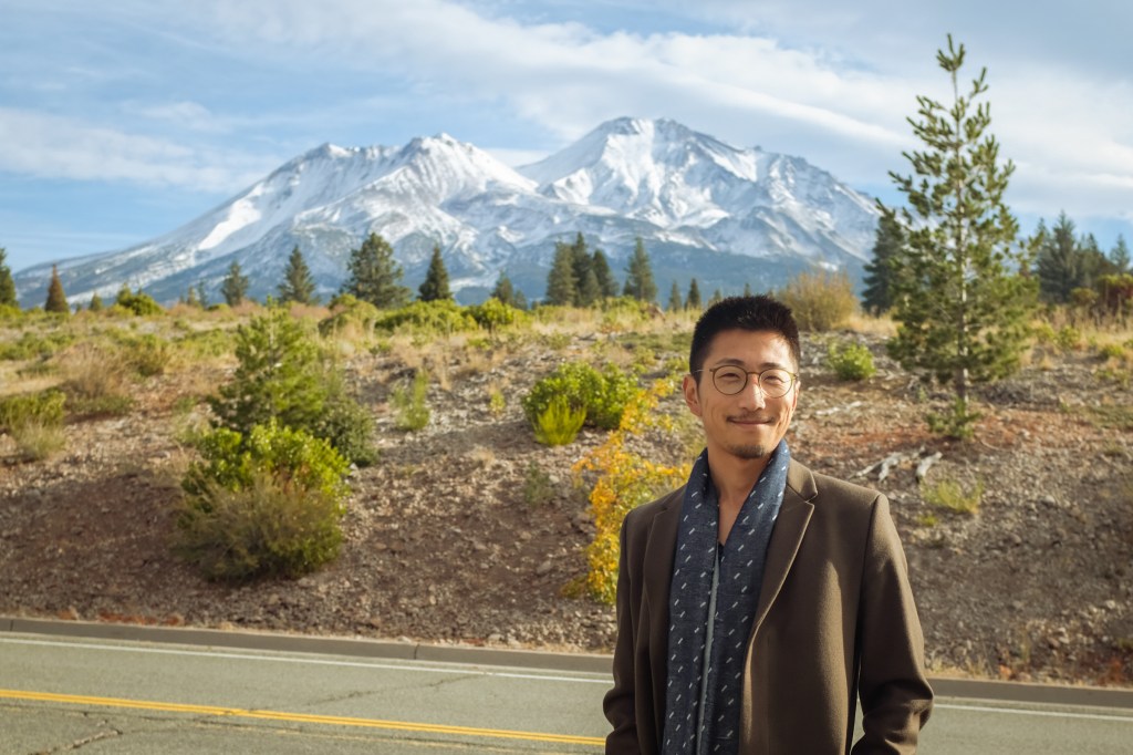 A man smiles before a snow-capped mountain