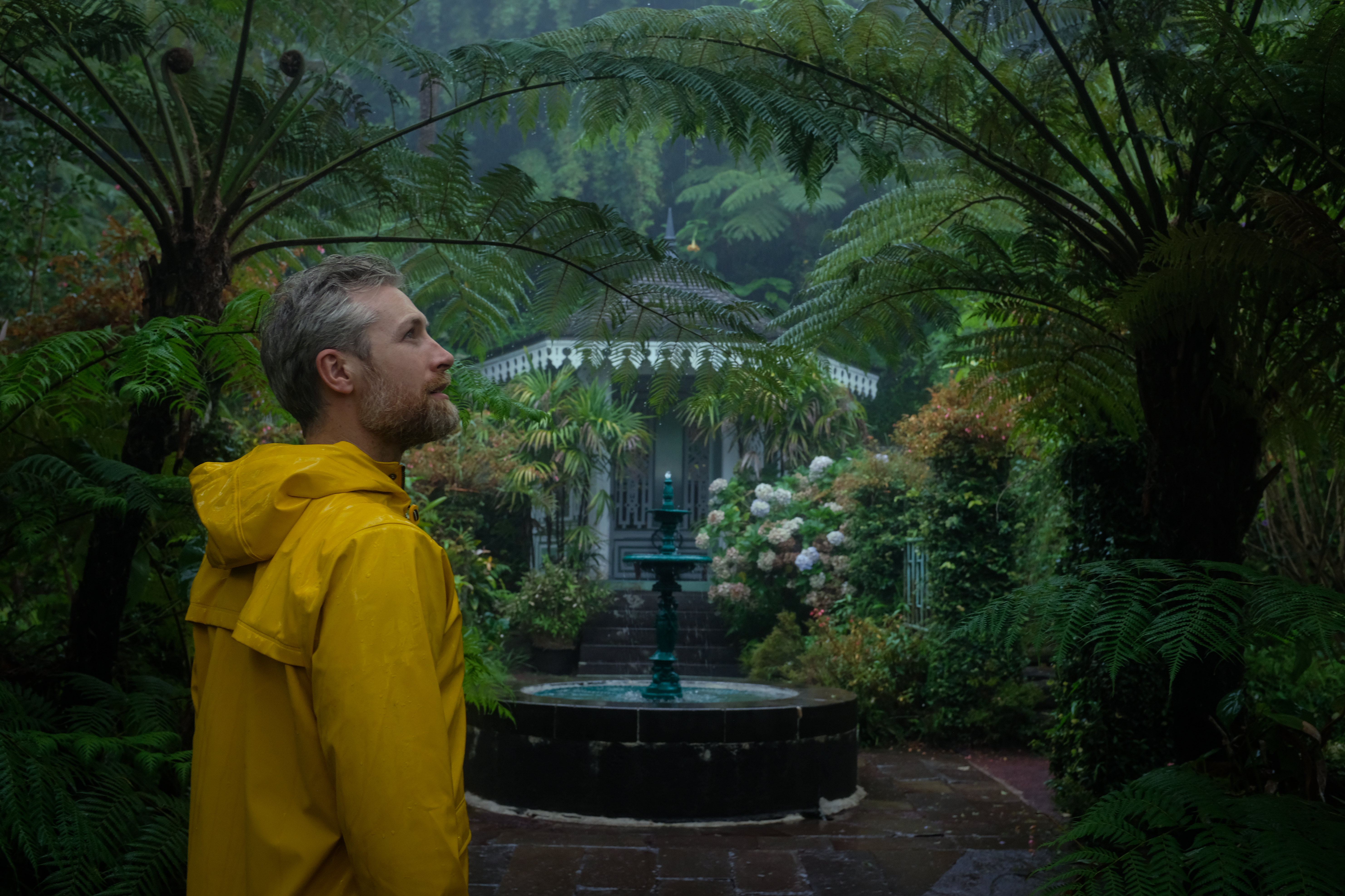 Man in rain jacket stands in front of a fountain and gazebo