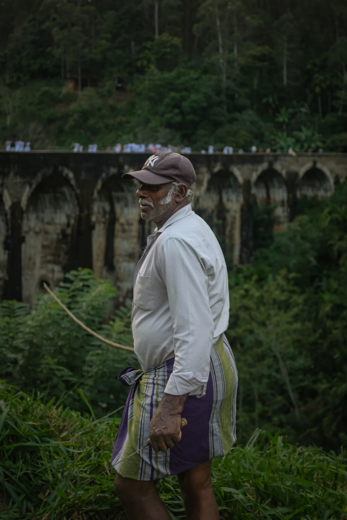 A man in sarong and cap walks in front of a colonial-era railway