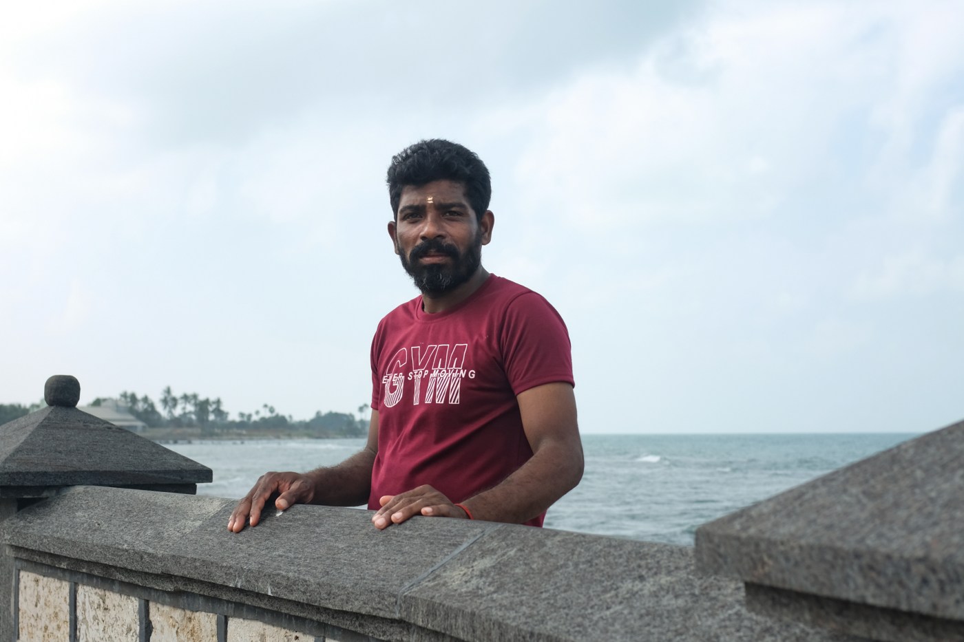 A Tamil man poses next to a wall by the ocean
